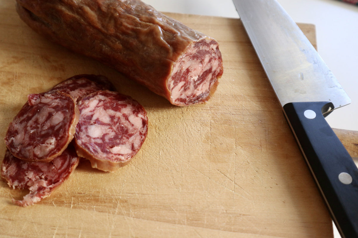 Salchichón cular ibérico de bellota cortado en rodajas sobre tabla de madera