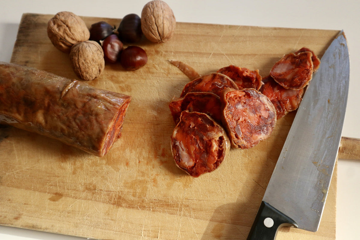 Chorizo cular ibérico de bellota en rodajas sobre tabla con nueces y castañas