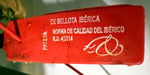 Precinto rojo oficial de la paleta de bellota ibérica, con el texto «PALETA, de bellota ibérica» y la referencia a la Norma de Calidad del Ibérico R.D. 4/2014.