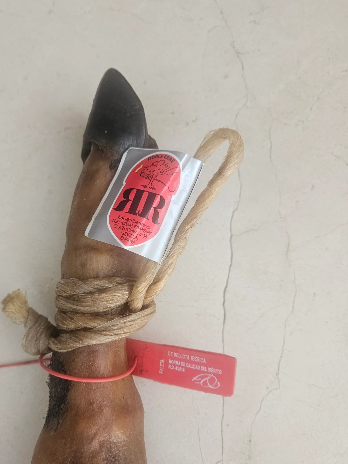 Detalle de la caña de la paleta de bellota 50% raza ibérica: etiqueta RR Doble Erre y precinto rojo con el texto «PALETA, de bellota ibérica, Norma de Calidad del Ibérico R.D. 4/2014».